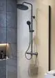 Duschsystem von Ideal Standard mit Kopfbrause und Handbrause in Silk Black, montiert an einer grauen Wand mit Beleuchtung im unteren Bereich und Handtuchablage.